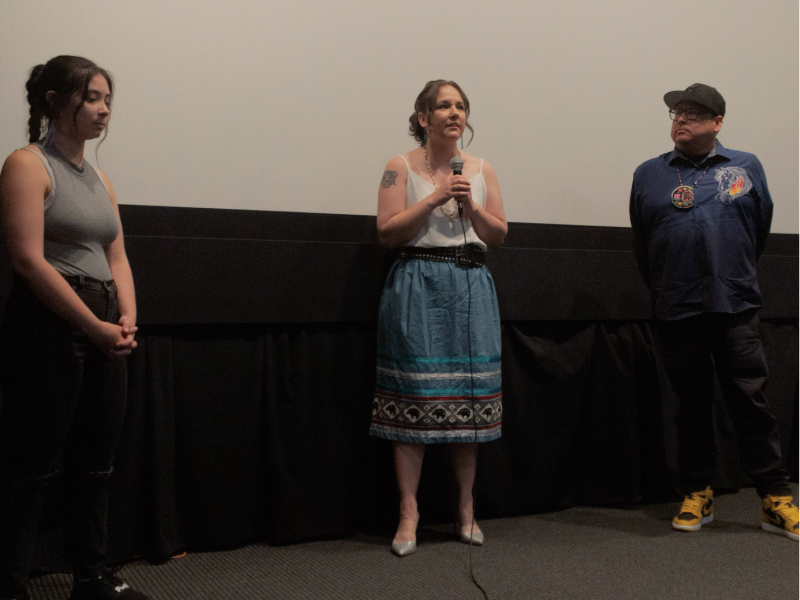 A photo of a mediator and two individuals being interviewed in front of a cinema screen at a film festival. 